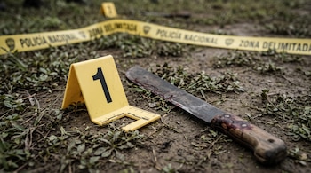 Un marcador amarillo de evidencia con el número uno y un machete con sangre sobre tierra, junto a una cinta de la Policía Nacional.