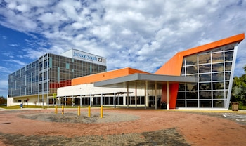 Edificio moderno de Jackson South Community Hospital con fachada de vidrio y detalles naranjas, entrada cubierta, pavimento de ladrillo y cielo con nubes