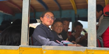 Una niña con gafas y varios niños miran a través de la ventana abierta de un autobús amarillo