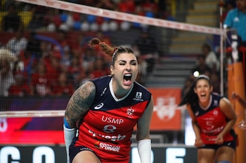 Primer plano de una jugadora de voleibol de la USMP gritando de emoción en la cancha, con tatuajes en el brazo y otra jugadora en el fondo