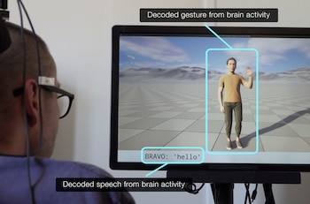 Un hombre con sensores en la cabeza mira un monitor que muestra un avatar digital levantando la mano y texto decodificado