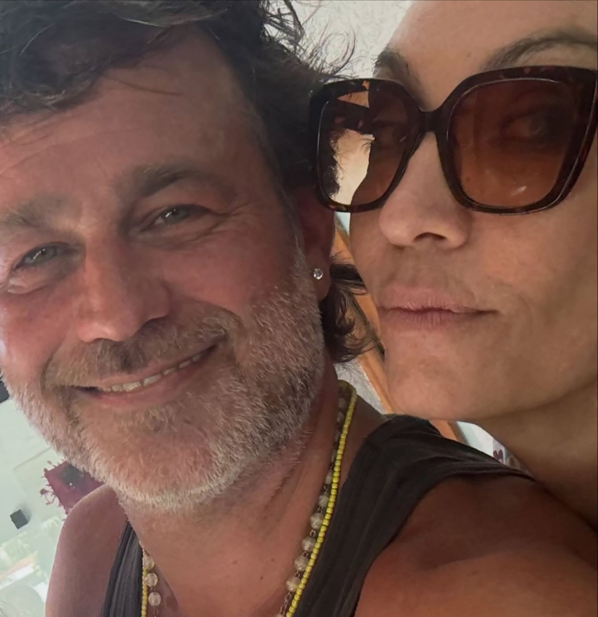 Una pareja se retrata en una selfie de primer plano donde el hombre sonríe y la mujer usa gafas de sol.