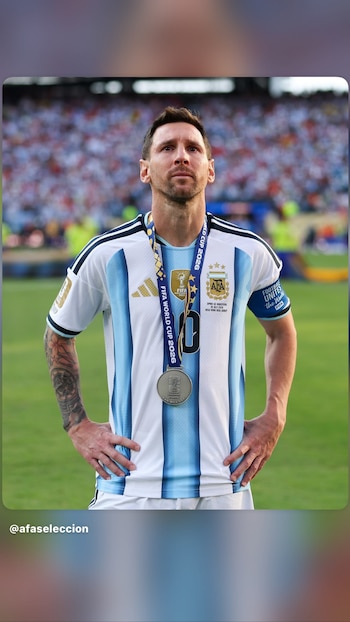 Primer plano de Lionel Messi, futbolista, vistiendo camiseta argentina rayada, con una medalla plateada en el cuello y tatuajes en el brazo izquierdo