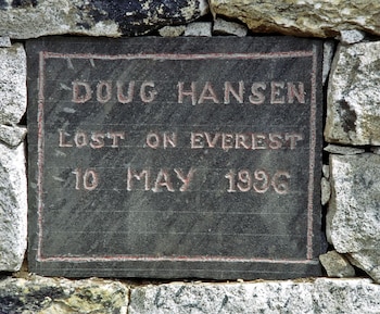Placa conmemorativa de piedra oscura con el nombre "DOUG HANSEN" y "LOST ON EVEREST 10 MAY 1996" grabado en rojo, incrustada en una pared de rocas