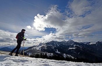 Eine Bergwandererin geht bei stürmischem Wetter vor der Kulisse des Mangfallgebirges über ein Schneefeld.