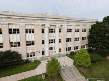 Fachada principal de la Perry Traditional Academy con columnas, múltiples ventanas, entrada, asta de bandera y escalinata. Rodeada de césped y árboles