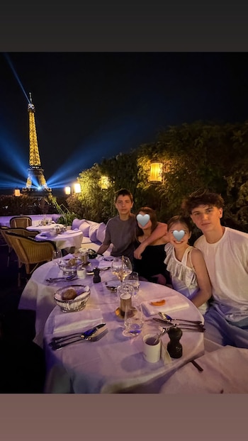 Cuatro de los hijos de Wanda Nara reunidos en la mesa del restaurante Girafe, con la Torre Eiffel iluminada de fondo. Los rostros de las niñas aparecen cubiertos con emojis de corazón