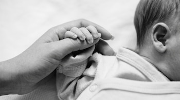 Fotografía en blanco y negro en plano cerrado de la mano de un bebé que sostiene el dedo de una persona adulta.