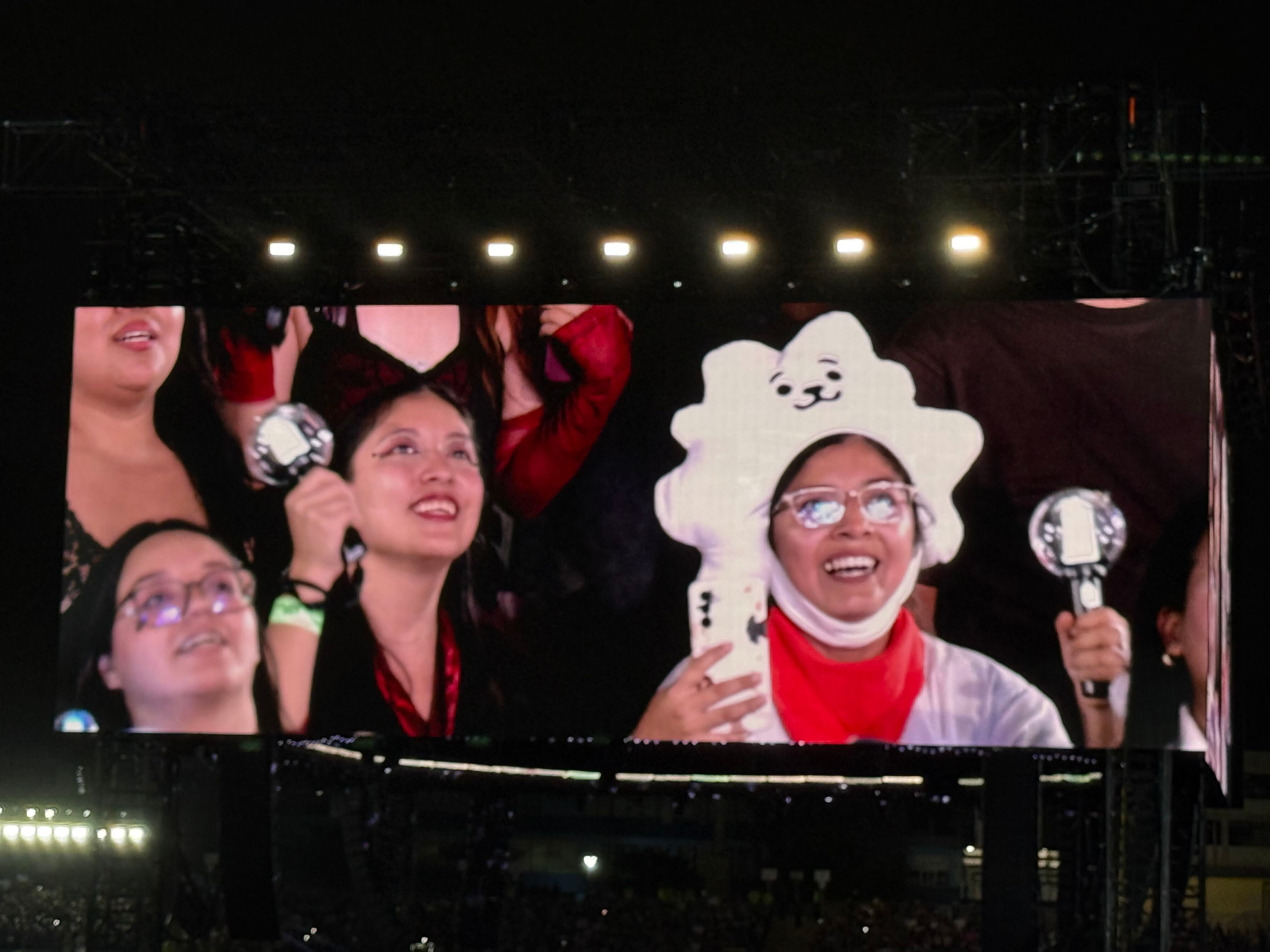 Seguidoras del grupo de K-pop BTS celebran con varas de luz proyectadas en una pantalla gigante durante un concierto en el Estadio San Marcos de Lima. (Paula Diaz)