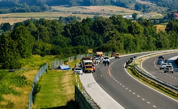 Autopista con vehículos detenidos en el arcén y conos de tráfico. Personas presentes. Carpa azul y blanca en la zona verde junto a la vía