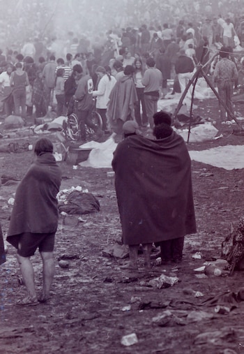Fotografía monocromática de una multitud de personas al aire libre en un terreno embarrado. Algunos individuos visten mantas y se observa una silla de ruedas