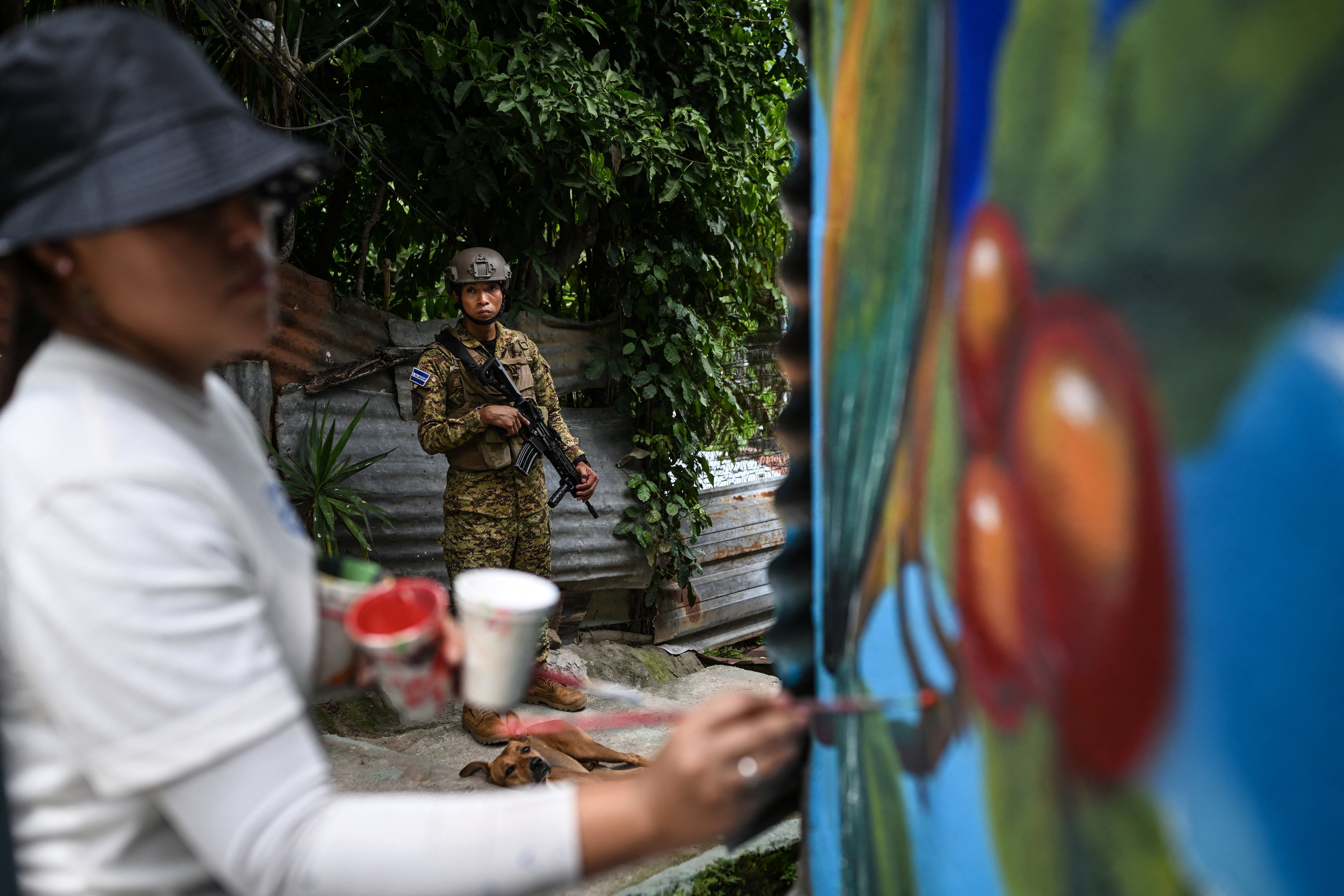 Un soldado salvadoreño monta guardia en la comunidad 10 de Octubre de San Marcos, El Salvador, mientras la artista Elizabeth Guardado pinta el mural