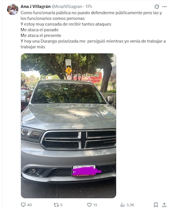 Una camioneta Dodge Durango plateada estacionada de frente en la calle. Se observa parte de la calle, árboles y una señal de tránsito