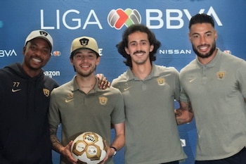 Cuatro hombres sonríen y posan frente a un logo de Liga BBVA. Uno de ellos, con gorra, sostiene un balón de fútbol blanco y dorado