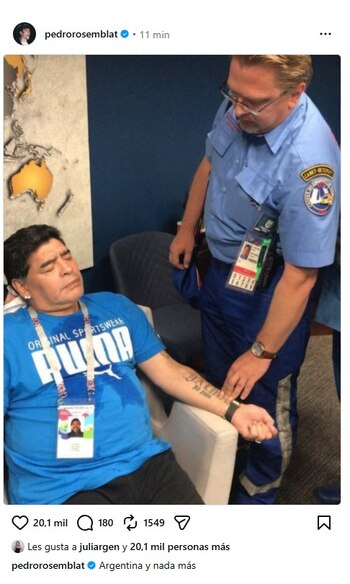 Diego Maradona sentado con ojos cerrados recibe asistencia de un hombre con uniforme paramédico. Se observa un mapa mundial en la pared
