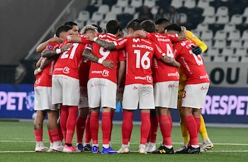 Jugadores de fútbol con uniforme rojo y blanco abrazados en un círculo sobre el césped de un estadio