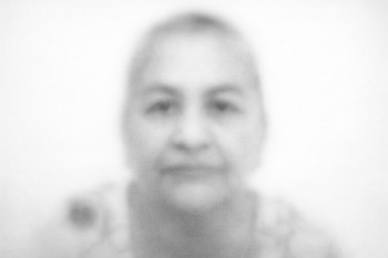 Primer plano borroso de la cabeza y los hombros de una mujer, en escala de grises y con un fondo blanco liso.