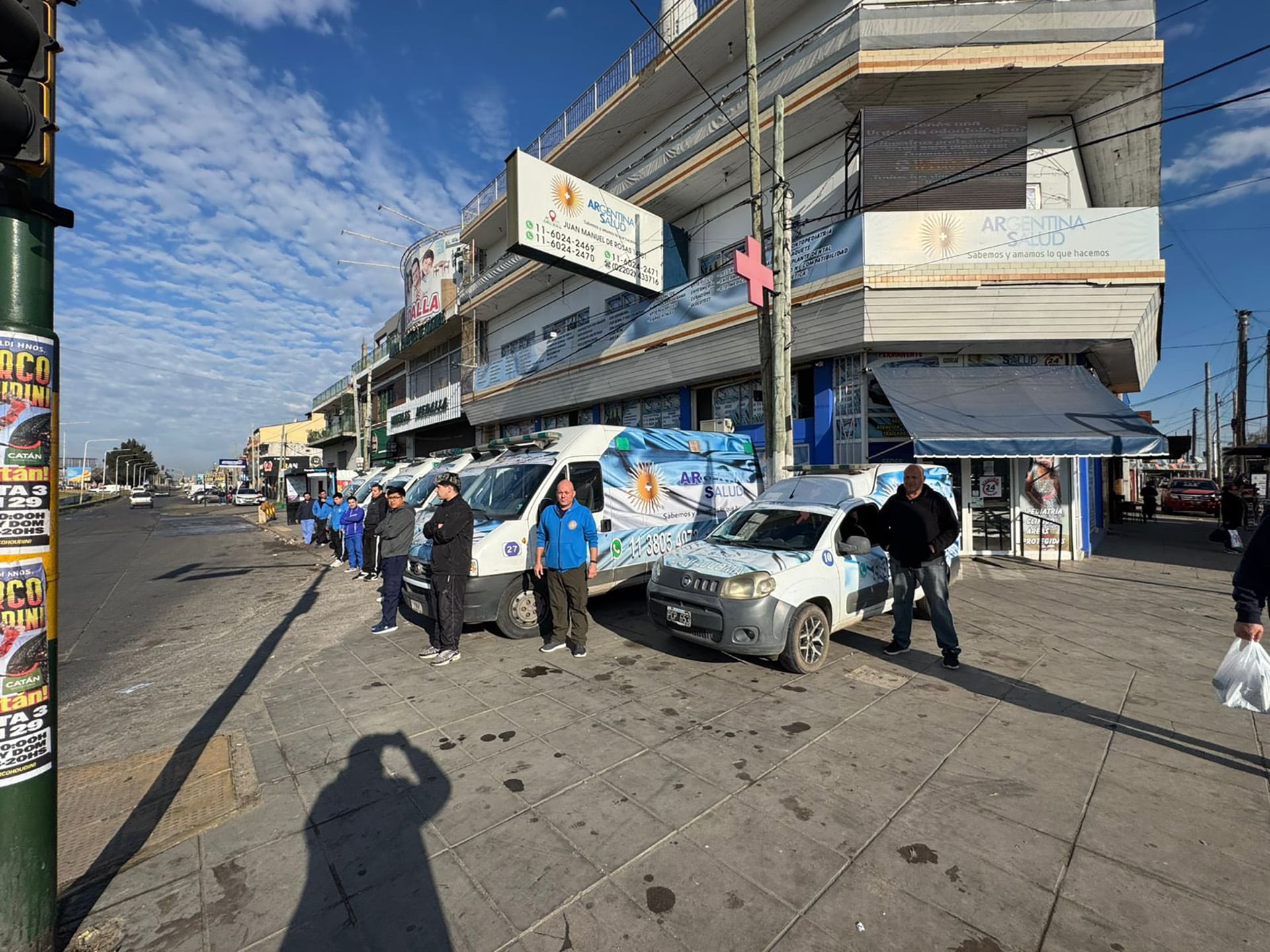 Personal de Argentina Salud se reúne junto a una fila de vehículos de servicio y un coche subcompacto marcados con el logo de la empresa, preparados en la vía pública frente a las oficinas de la organización.
