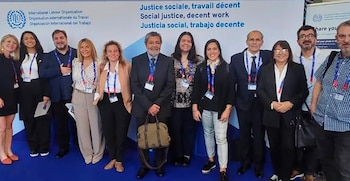 Grupo de once personas, seis mujeres y cinco hombres, de pie sonriendo ante un fondo blanco con el logo de la OIT y la frase 'Justicia social, trabajo decente'