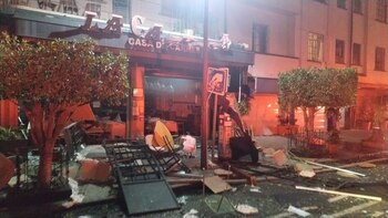 Fachada de un restaurante con el letrero "La Casa Di Carnes" dañada, escombros, mesas, sillas y objetos dispersos en la acera frente al local