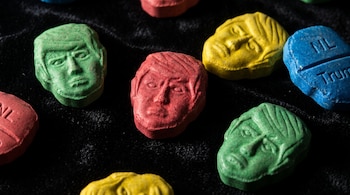 Pastillas de colores verde, rojo, amarillo y azul con el rostro de Donald Trump sobre una tela negra.