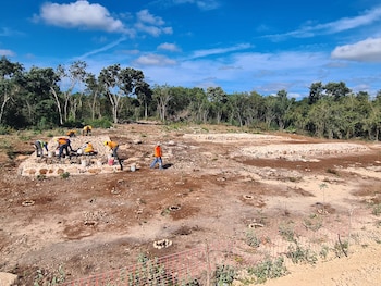 Trabajadores con chalecos de seguridad y cascos consolidan estructuras de piedra en el sitio arqueológico de Chichan Panadero, Yucatán, bajo un cielo azul y árboles