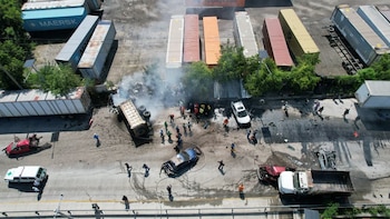 Varios socorristas con uniformes blancos y rojos inspeccionan un automóvil negro destruido junto a la estructura de un camión