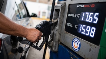 Mano que sostiene una pistola de combustible en un automóvil junto a una pantalla con precios de gasohol y diésel de Petroperú.