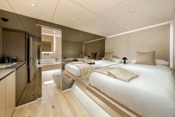 Dormitorio con dos camas individuales, pared de espejos, muebles de madera clara y un baño contiguo con lavabo e inodoro