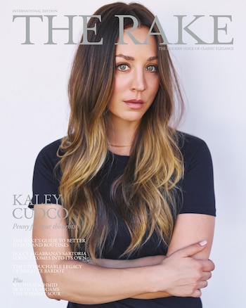 Retrato de Kaley Cuoco en la portada de The Rake, con cabello castaño claro, ojos verdes, camiseta negra y brazos cruzados, mirando a cámara