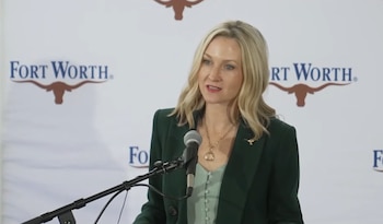 Mattie Parker, mujer de cabello rubio y chaqueta verde, habla ante un micrófono frente a un panel de la ciudad de Fort Worth