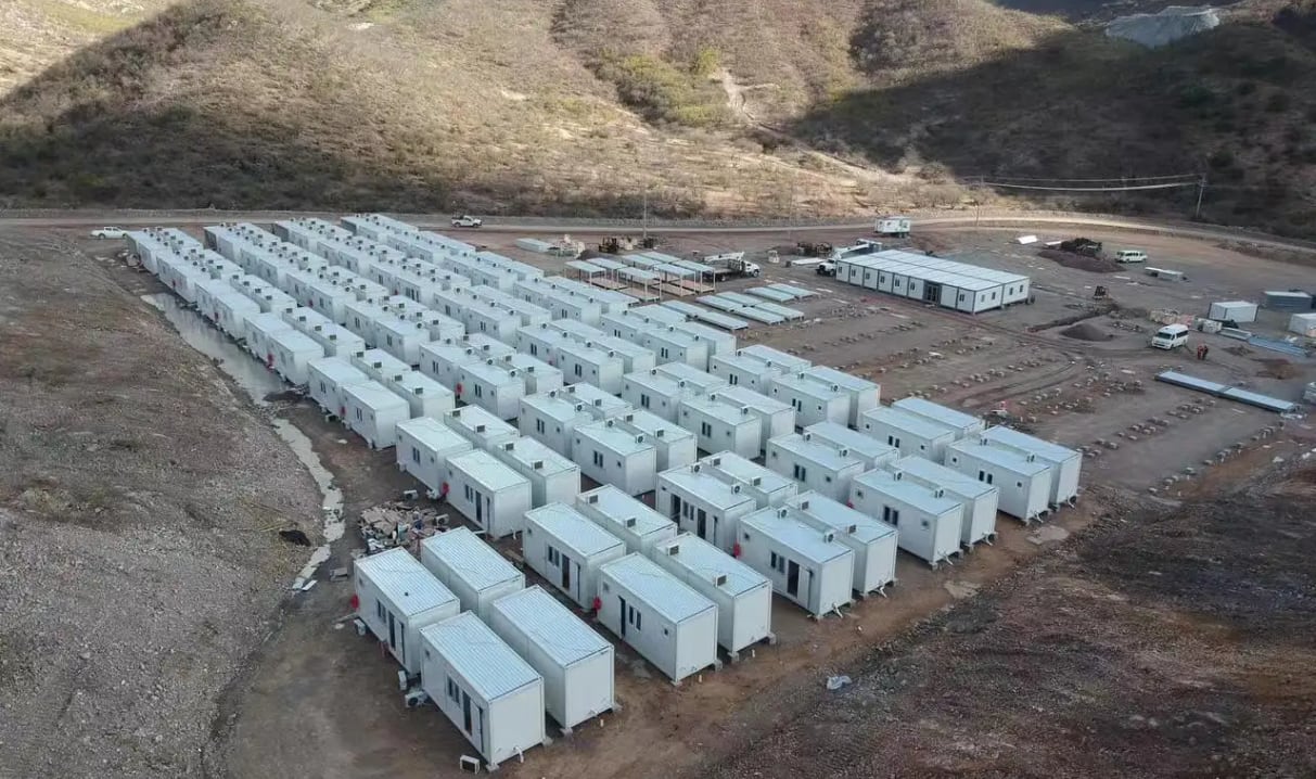 Vista aérea de un extenso campamento de unidades modulares blancas, parte de una instalación minera, situado en un terreno árido y montañoso (Chengdong Housing)