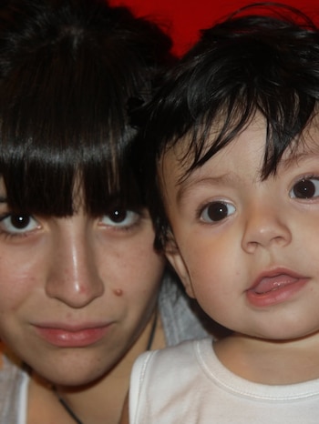 Primer plano de Gianinna Maradona con cabello oscuro y flequillo, sonriendo levemente, junto a su hijo Benjamín Agüero, un niño de pelo oscuro con boca entreabierta
