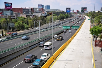 Vista aérea de una autopista con múltiples carriles y tráfico denso. A la derecha, un carril lateral recién pavimentado y vacío junto a una barrera amarilla