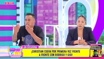 Christian Cueva en un set de televisión, gesticulando con las manos. Una mujer sentada a su derecha viste blazer oscuro. Pantallas con luces de colores al fondo