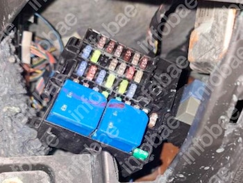 Caja de fusibles eléctricos de un automóvil con piezas de varios colores, dos relés azules y cables en el fondo