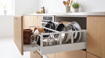 Cajón de cocina abierto de madera con ollas, sartenes, tapas y cuencos ordenados en separadores.