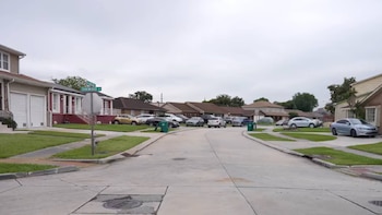 Calle residencial despejada con casas de una o dos plantas, múltiples coches aparcados, aceras de hormigón y bordillos, y un cartel de calle "Oakwood"