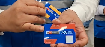 Manos de una persona sujetando dos tarjetas de transporte azules y rojas. Las tarjetas tienen logos de Perú y ATU, y el texto "Pase Libre Policía-Bombero"