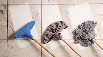 Tres mangos de madera con paños azul, rayado y gris reposan sobre baldosas sucias que tienen tres rectángulos limpios.