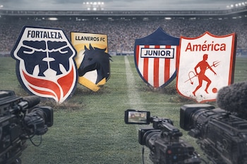 Un campo de fútbol con cuatro escudos de equipos: Fortaleza, Llaneros FC, Junior y América. Dos cámaras de televisión frente a ellos y un estadio con público al fondo.