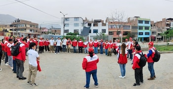 Un grupo numeroso de personas, muchas vistiendo chaquetas rojas y blancas, se reúne en un círculo al aire libre en un área urbana con edificios