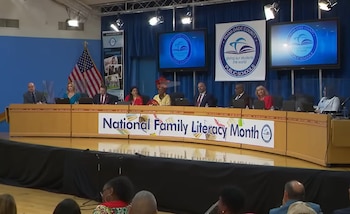 Panel de oficiales sentados detrás de una mesa curvada de madera en una sala de reuniones, con una bandera de Estados Unidos y pantallas con logos de Escuelas Públicas de Miami-Dade