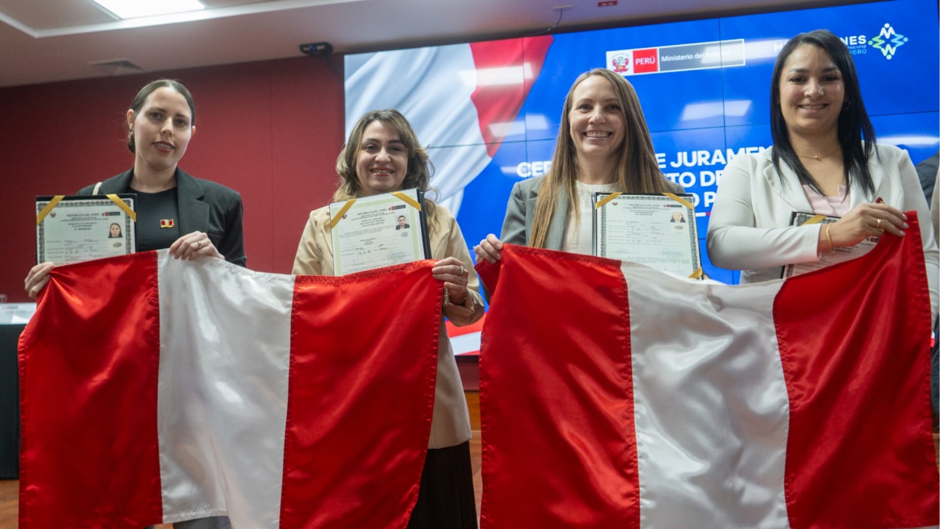 Cuatro de las personas nacionalizadas sostienen sus títulos y la bandera peruana durante la ceremonia organizada por Migraciones en Jesús María. (Migraciones)
