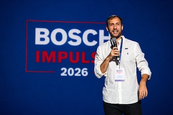Un hombre de barba y camisa blanca con un micrófono habla en un escenario azul. Detrás, un panel dice 'Bosch Impulsa 2026' en letras grandes