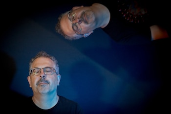 Primer plano de un hombre con lentes y goatee, ojos cerrados. Arriba, el reflejo invertido de un hombre con lentes, ojos abiertos. Fondo azul oscuro