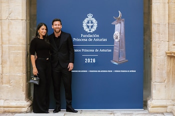 Un hombre y una mujer vestidos de negro posan junto a un panel azul con emblemas institucionales flanqueado por columnas de piedra