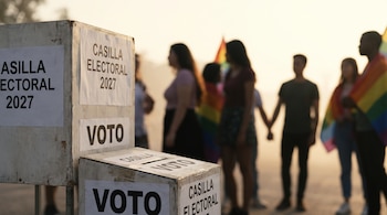 Dos casillas electorales de madera, una con las inscripciones 'CASILLA ELECTORAL 2027' y 'VOTO'. Siluetas borrosas de personas, algunas con banderas arcoíris.