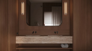 Vista frontal de un baño moderno con paredes de madera. Incluye un espejo grande, doble lavabo de piedra, grifos negros y dos apliques de luz.