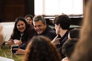 Sergio Massa sentado a una mesa mientras sostiene un mate, rodeado por varias personas jóvenes